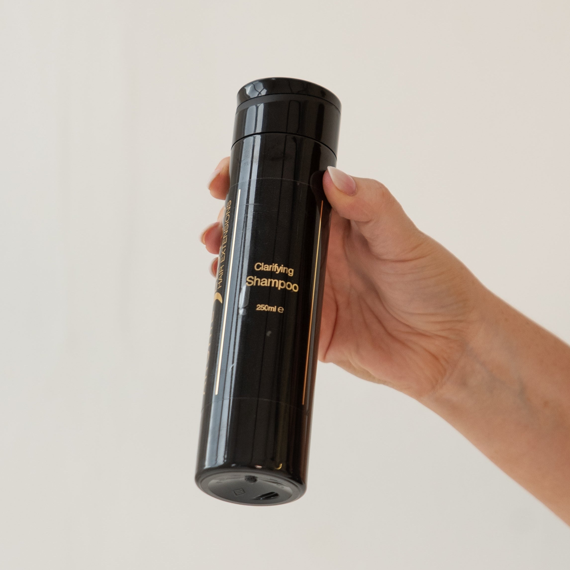 Hand holding a black shampoo bottle labeled 'clarifying shampoo' on a light background
