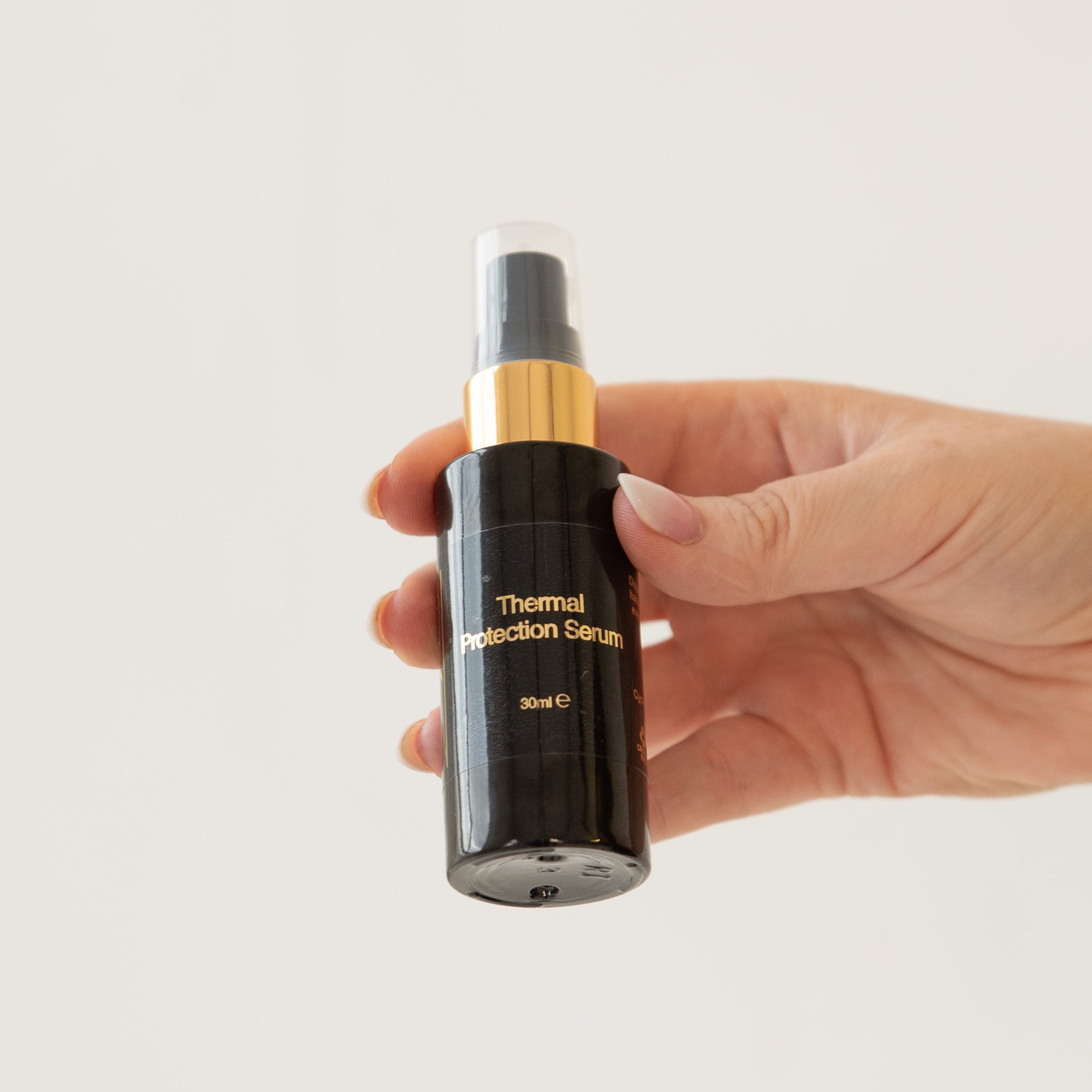 Hand holding a black serum bottle with gold cap on a light gray background