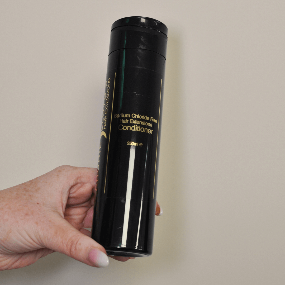 Hand holding a black conditioner bottle labeled 'Nexxus' on a beige background