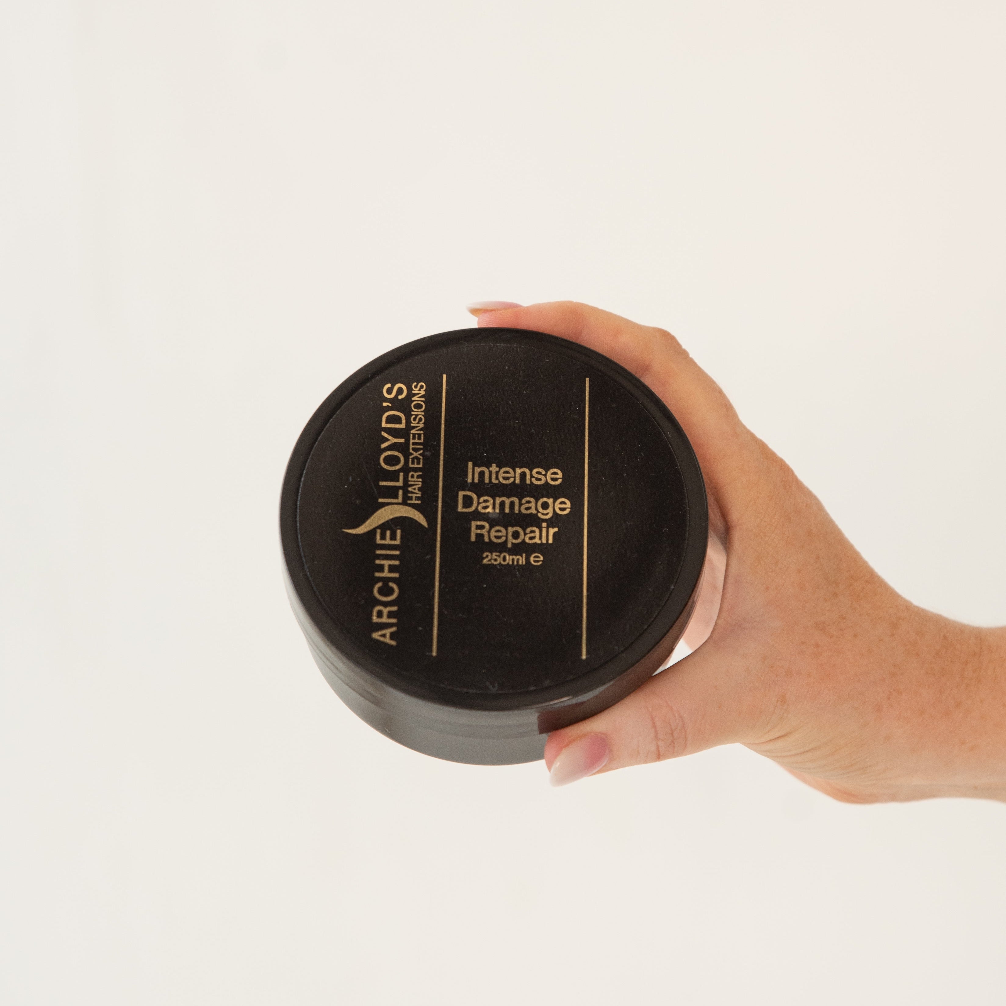Hand holding a jar of Archie Lloyd's Intense Damage Repair product on a light background