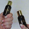 Two black bottles with gold caps held by a person against a white background