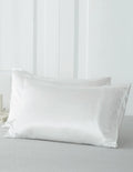 Two white satin pillowcases on a bed, designed for hair extension care.
