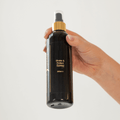 Hand holding a black spray bottle labeled 'Shake & Protect Spray' on a light gray background